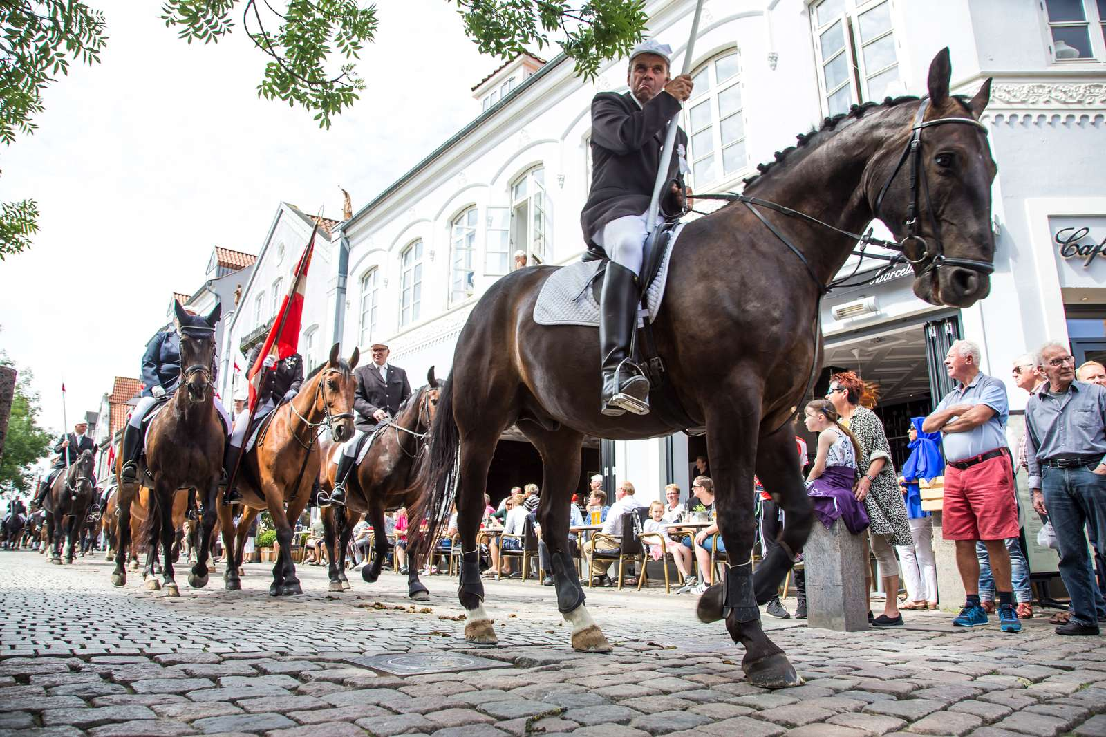 Ringridning i Sønderborg — ryttere i traditionelle uniformer på hestebag gennem byens brostensgader, omgivet af tilskuere