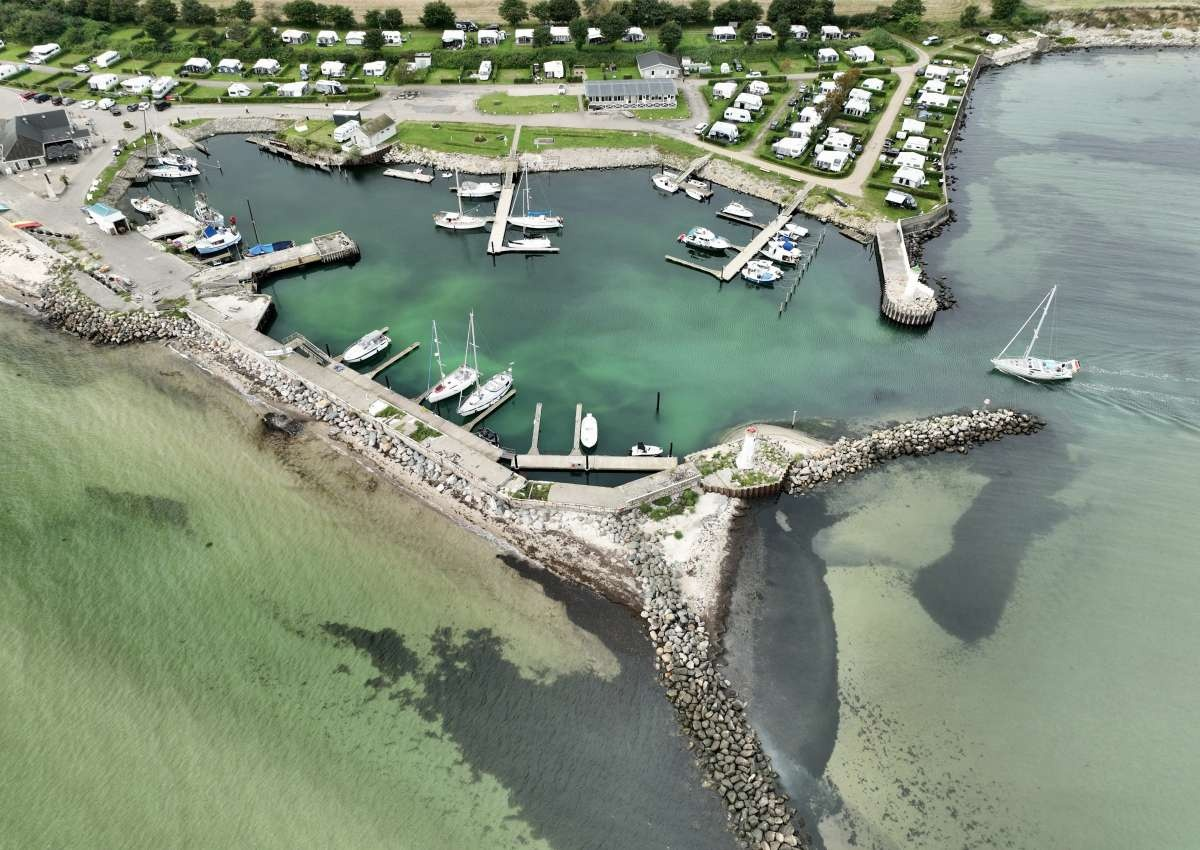 Mommark Marina — luftfoto af lystbådehavn med klart turkisgrønt vand, sejlbåde langs broerne, campingplads i baggrunden og stenede moler mod Østersøen