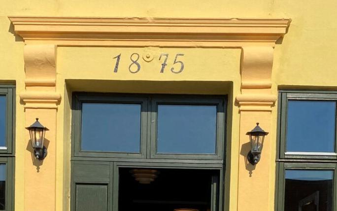 Skovby Kro, gul krokrygge fra 1875 med grønne døre, lanterner og danske flag