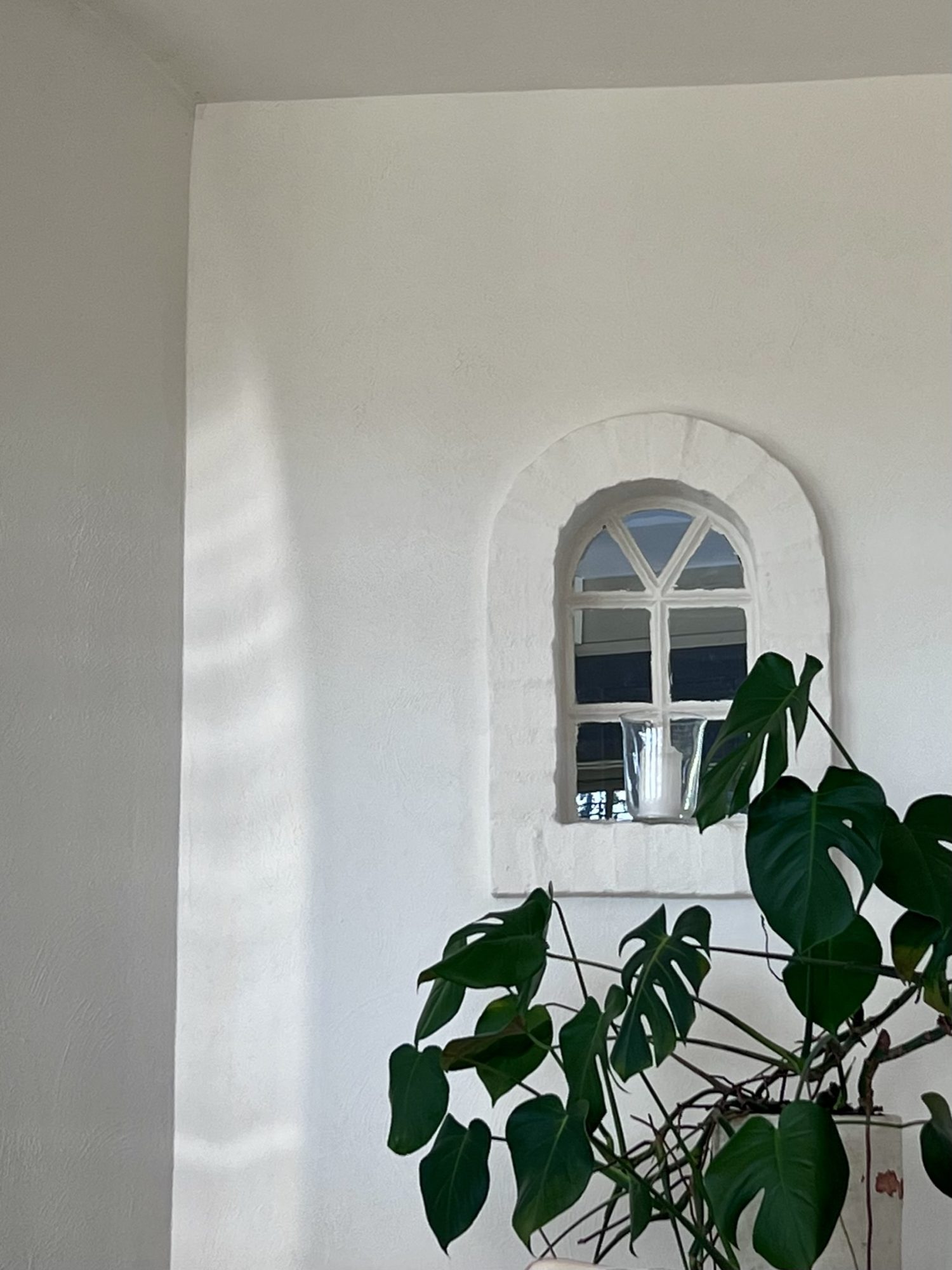 Hvid væg med buet vindue og monstera