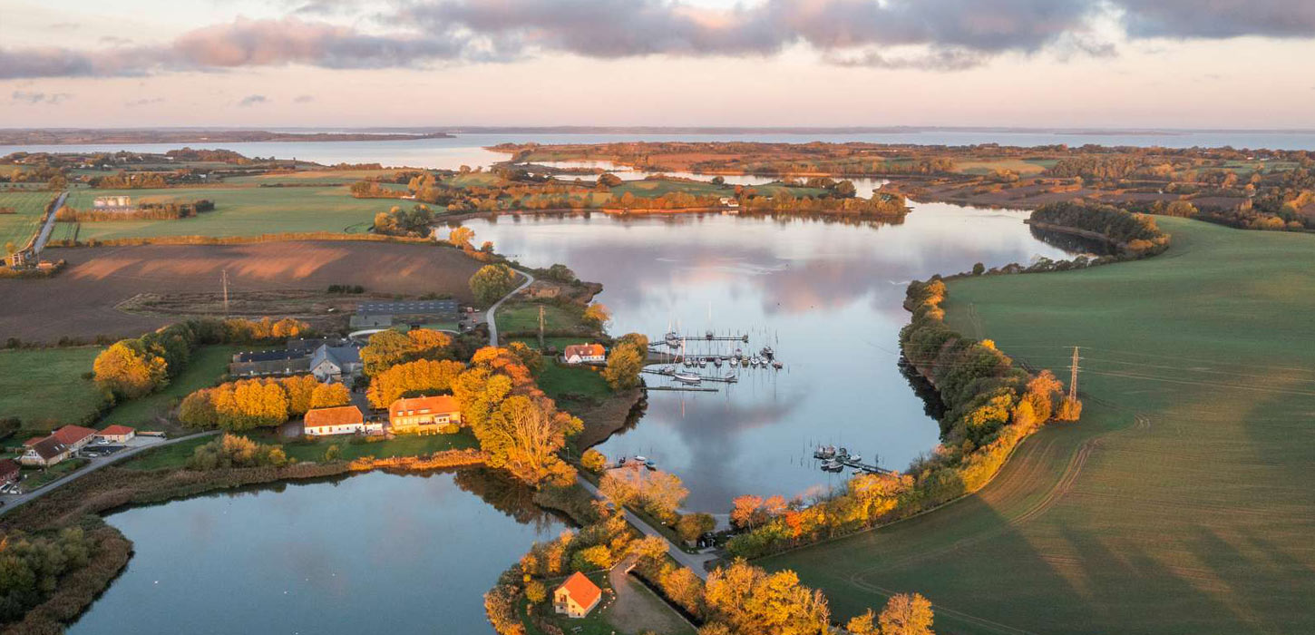 Naturpark Nordals — luftfoto af smukke søer og bugter omgivet af gule efterårstræer, grønne marker og små rødtagehuse med sejlbåde i havnen og vid udsigt over vandet i aftenslys
