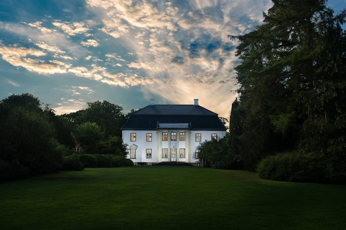 Augustenborg Slot — hvidt palæ med sort tag i aftenslys, omgivet af park
